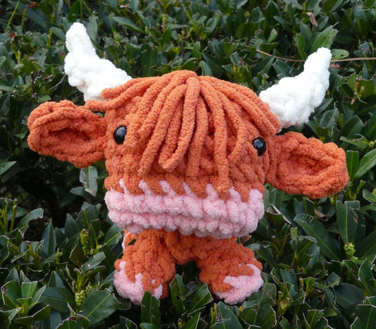 An amigurumi highland bull made with soft Bernat Blanket yarn in pumpkin spice with a pink nose and feet and white horns.